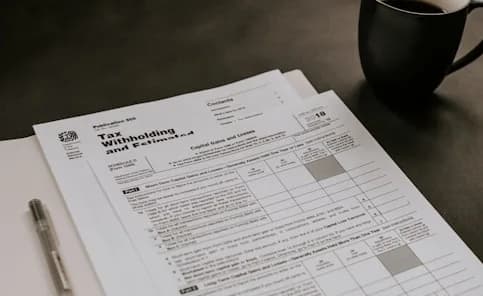 Tax forms on a desk beside a pen and a cup of coffee
